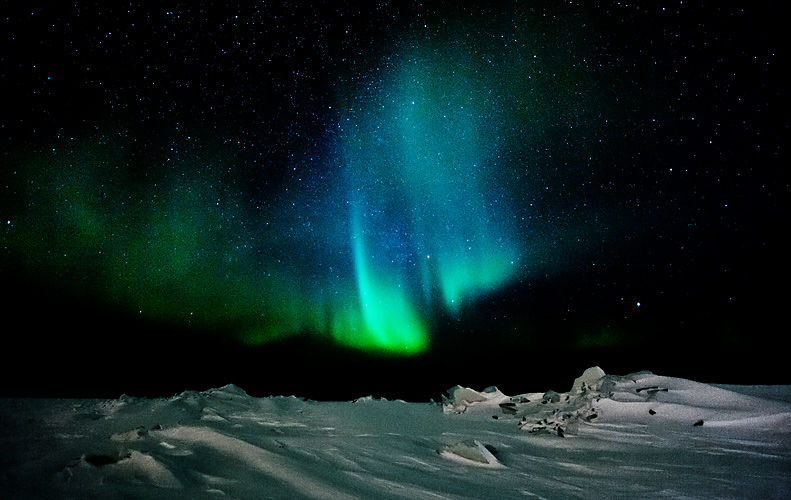 Bursts of greenish-blue color from the Northern Lights illuminate the night sky above the Great Slave Lake in Northwest Territories.
